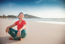 Beautiful Mature Woman 50 Years Old Resting In Lotus Position On The Beach By The Sea. Active Lifestyle, Travel And Sport For Senior Citizens