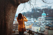 A young woman tourist photographs on a telephone a panorama of the medieval city of Salzburg.Very beautiful view of the winter Salzburg, the cathedral and the Hohensalzburg fortress, Austria