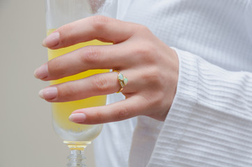 A beautiful expensive  iridescent wedding ring with tiny diamonds on a smooth woman hand holding orange champagne. Photographed with a shallow depth of field.