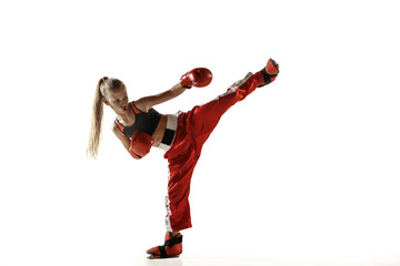 Young female kickboxing fighter training isolated on white background. Caucasian blonde girl in red sportswear practicing in martial arts. Concept of sport, healthy lifestyle, motion, action, youth.