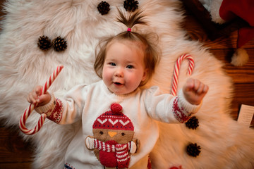 7 month old girl in a red Christmas costume on a background of retro garlands sits on a fur