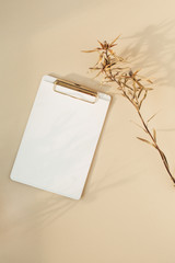 Wall Mural - Blank paper clipboard with empty copy space and dry flower branch on pastel beige background. Flat lay, top view minimal home business template for social media, blog, website.