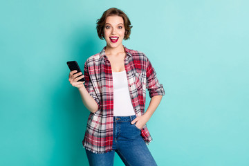 Wall Mural - Portrait of astonished girl blogger use smart phone get social network notification impressed scream wow omg wear stylish outfit denim isolated over teal color background