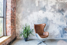Chair in front of the grunge gray wall. Big window. Empty loft style room
