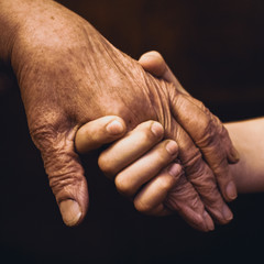 The hands of an old grandmother and a child touch in a handshake for support and help.