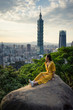 © Juan Alberto Ruiz/ADDICTIVE STOCK - Tranquil female traveler in stylish yellow dress sitting in big rock while enjoying in views with city plants and sky on background in Scotland