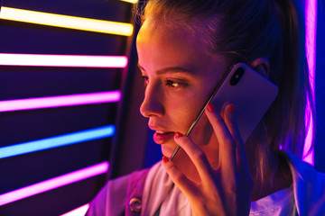 Image of woman talking on smartphone by multicolored neon lights indoors