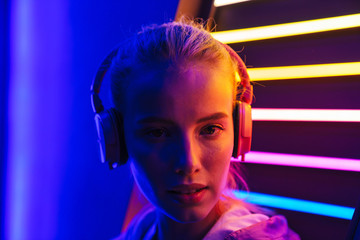 Wall Mural - Image of woman listening to music with headphones over neon illumination