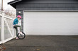 © Cavan Images - Girl in Pink Helmet Looking Down at Unicycle in Front of Garage Door