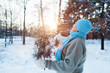 Winter seasonal activities. Senior woman throwing snow in the air at sunset in forest holding fir tree branches