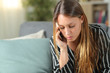 © Antonioguillem - Serious woman talking on phone on a sofa at home