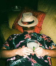 Male In Tropical Shirt Drinking Cocktail Asleep On Couch