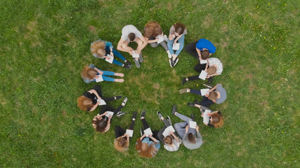 A group of students are sitting in a circle and books on the grass.