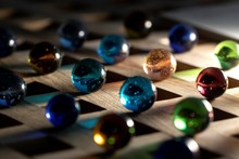 A Portrait Of A Lot Of Different Marbles In Different Colors, Lying On A Wooden Roster Casting A Colorful Shadow Onto The Wooden Surface.