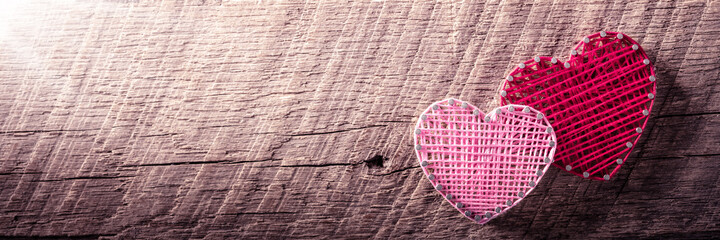 Wall Mural - banner of two heart shapes made of yarn and nails on rustic wooden background with sunlight - valent