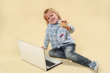 Wondered baby looks at notebook screen. Business kid with a golden bank card and money. Concept of business, success and online computer work. In the studio on an orange background. Copy spase