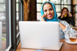 © Westend61 - Businesswoman wearing turquoise hijab in a cafe and working with her laptop, on the phone