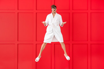 Poster - Jumping young man in bathrobe and with coffee on color background