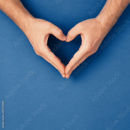 Male hands in shape of heart on classic blue background. Healthcare and chirt...
