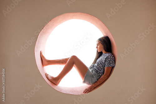 Cuadros en Lienzo Young barefoot girl curled inside a round opening