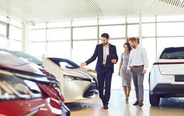 Couple and the dealer selling cars look the car in the showroom.