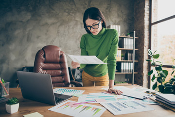 Photo of beautiful busy business lady notebook table paper stats on table analyzing money income standing near chair wear specs green turtleneck yellow pants modern office