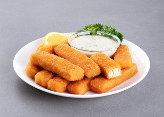 Wall Mural - Fish fingers sticks on a plate with parsley, lemon and tartar sauce on a gray texture.