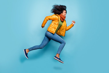 Wall Mural - Full length profile photo of beautiful dark skin lady jumping high running sale shopping rushing wear overcoat jeans green sweater scarf isolated blue color background