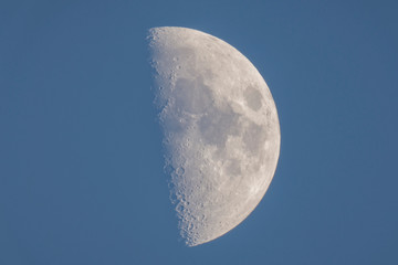 Wall Mural - moon showing first half in late afternoon blue sky, cornwall, uk