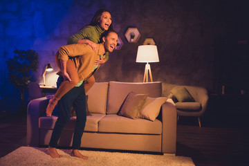 Wall Mural - Full length body size view of his he her she nice attractive glad cheerful cheery spouses piggy-backing having fun spending free time at night home house living-room apartment indoors