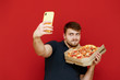 © bodnarphoto - Funny bearded man taking selfie with pizza box on red background, looking at smartphone and making funny face. Cheerful man taking photo with pizza delivery box. Isolated.