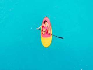 Wall Mural - Attractive woman in swimwear floating on stand up paddle board on a quiet blue ocean. Sup surfing in tropical sea