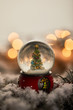 little snowball with christmas tree standing on spruce branches in snow with golden lights bokeh