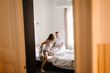 © Serhii - Love couple beats pillows lying in bed, view through the door. A Satisfied and happy woman jumps with her husband. Emotions of happiness beautiful young couple. Lifestyle.