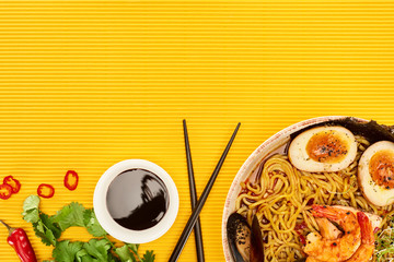 Wall Mural - top view of seafood ramen near fresh ingredients, soy sauce and chopsticks on yellow surface