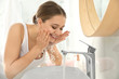 © New Africa - Young woman washing face with tap water in bathroom