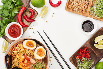 Wall Mural - top view of spicy seafood ramen near fresh ingredients and chopsticks on white surface