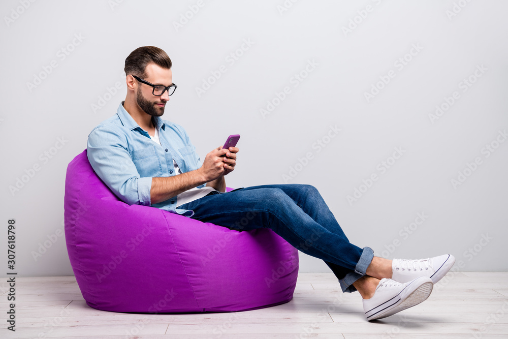 Full size profile photo of crazy guy sitting comfy soft violet armchair holding telephone chatting colleagues wear specs casual denim outfit isolated grey color background - obrazy, fototapety, plakaty 