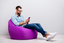 Full Size Profile Photo Of Crazy Guy Sitting Comfy Soft Violet Armchair Holding Telephone Chatting Colleagues Wear Specs Casual Denim Outfit Isolated Grey Color Background