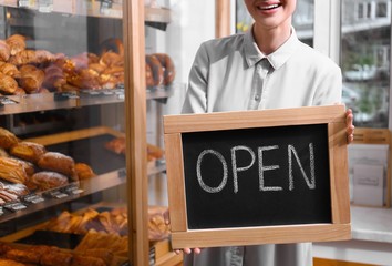 Wall Mural - Female business owner holding OPEN sign in bakery, closeup