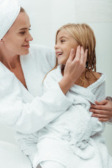 happy mother touching face of cute daughter in bathroom