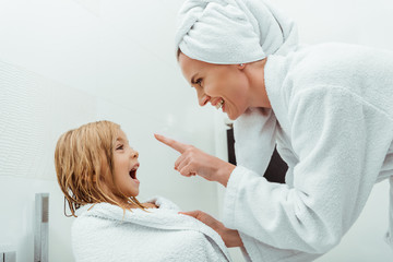 happy mother pointing with finger near excited daughter in bathroom