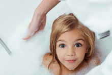 Overhead View Of Happy Kid Taking Bath And Looking At Camera Near Mother