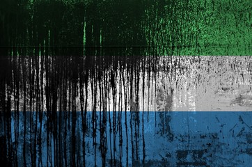 Sierra Leone flag depicted in paint colors on old and dirty oil barrel wall closeup. Textured banner on rough background