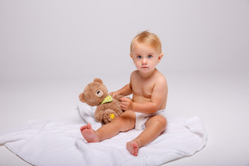 a little girl baby in a diaper holding a teddy bear sitting on a white background.