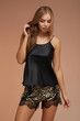Medium full shot of a slim blonde lady in a silk home lingerie set consists of easy fit shorts and a black loose t-shirt. The shorts with leopard print are decorated with black fancy lace. 