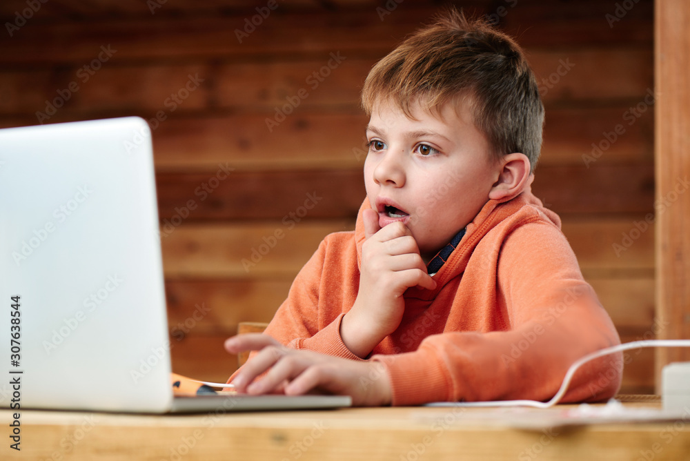 Shocked child boy with open mouth and bulging eyes looks at a computer laptop screen. Internet porn censorship concept, adult content 18+ - obrazy, fototapety, plakaty 