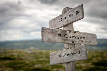decide commit and succeed text on wooden rustic signpost outdoors in nature/mountain scenery. lifest