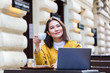 © Graphicroyalty - Young Asian woman sitting in coffee shop at wooden table, drinking coffee and using smartphone.On table is laptop. Girl browsing internet, chatting, blogging.