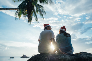 A guy and a girl are sitting on a stone at sunset on the beach in New Year's hats.